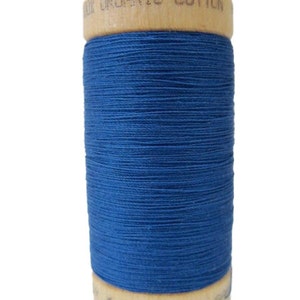 May include: A spool of blue organic cotton thread on a wooden bobbin. The bobbin is labeled "100% Organic Cotton" and "LOOM".