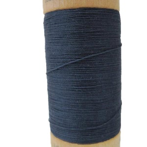 Puede incluir: Una bobina de hilo de algodón orgánico 100% azul oscuro en una bobina de madera. La bobina está etiquetada con "100% algodón orgánico" y "1000 Y/1000".