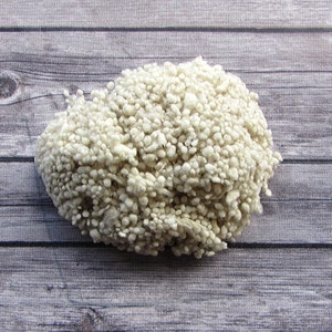 May include: A close-up of a pile of white fluffy yarn. The yarn is made of small, round balls of fiber.