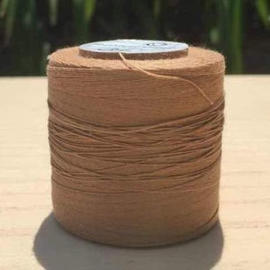 May include: A spool of brown waxed thread for leather crafting. The thread is wound tightly on a cardboard spool with a white label.