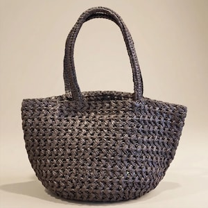 May include: A woven gray tote bag with a rounded base and two handles. The bag is made of a textured material with a basket-weave pattern. The handles are also woven and attached to the top of the bag.