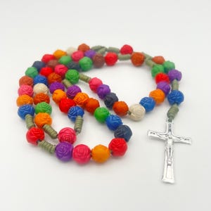 May include: A vibrant rosary with rose-shaped beads in a spectrum of colours, including red, orange, blue, green, and purple. The beads are strung on a green cord, ending with a silver crucifix.