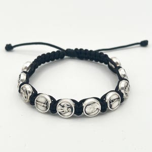 Puede incluir: Pulsera de cordón trenzado negro con abalorios circulares plateados. Cada abalorio presenta un símbolo religioso. La pulsera tiene un cierre de nudo corredizo ajustable. Un accesorio religioso sencillo y elegante.