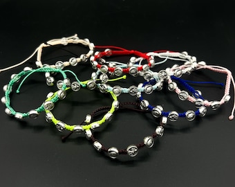 Puede incluir: Una colección de pulseras coloridas con cuentas plateadas y cordón. Cada pulsera presenta un cordón de diferente color, incluyendo blanco, rojo, verde, amarillo, marrón, azul y rosa. Las cuentas tienen un símbolo de la paz.