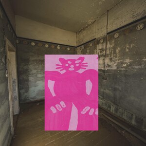 May include: A rectangular painting featuring a stylized, symmetrical cat figure rendered in two shades of vibrant pink. The cat has large, rounded ears, wide eyes, and prominent paws, set against a lighter pink background within the artwork.