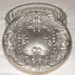 May include: A silver-plated round lid with an ornate design. The lid is for a glass jar or container.