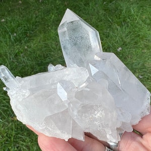 May include: A cluster of clear quartz crystals with a variety of sizes and shapes. The crystals are arranged in a natural formation, with some pointing upwards and others pointing downwards. The crystals are translucent and have a slight sparkle.