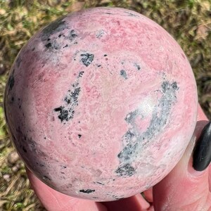 May include: A pink and black sphere of polished rhodochrosite, a type of crystal.