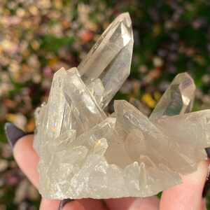 Puede incluir: Un c&uacute;mulo de cristales de cuarzo transparentes con destellos iridiscentes de arco&iacute;ris. Los cristales est&aacute;n dispuestos en un c&uacute;mulo, con algunos apuntando hacia arriba y otros hacia abajo. Los cristales son transl&uacute;cidos y tienen un aspecto v&iacute;treo.