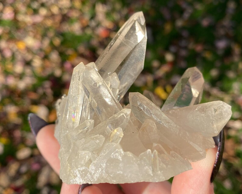 Puede incluir: Un c&uacute;mulo de cristales de cuarzo transparentes con destellos iridiscentes de arco&iacute;ris. Los cristales est&aacute;n dispuestos en un c&uacute;mulo, con algunos apuntando hacia arriba y otros hacia abajo. Los cristales son transl&uacute;cidos y tienen un aspecto v&iacute;treo.