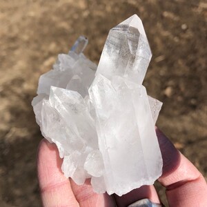 May include: A cluster of clear quartz crystals with a pointed shape. The crystals are arranged in a cluster, with the largest crystal in the center.