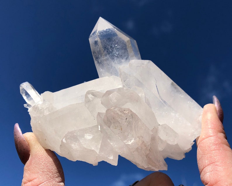May include: A cluster of clear quartz crystals with a variety of shapes and sizes. The crystals are arranged in a way that resembles a small mountain range. The crystals are translucent and have a slight sparkle.