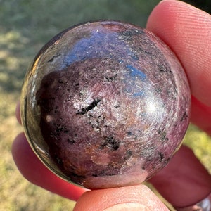 May include: A polished purple and black sphere crystal ball. The sphere is smooth and has a reflective surface.
