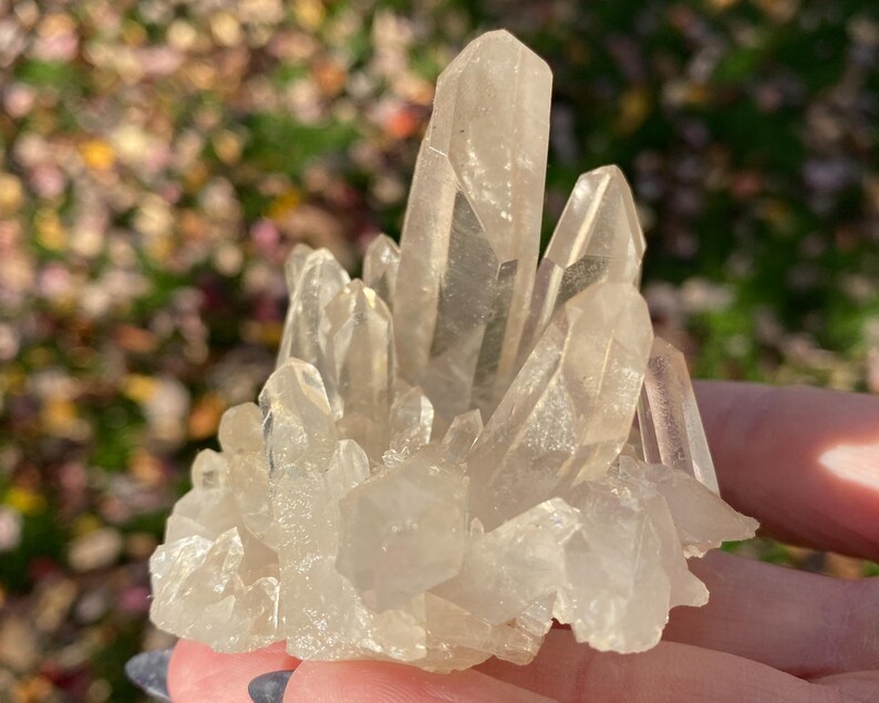 Puede incluir: Un c&uacute;mulo de cristales de cuarzo transparentes de diferentes tama&ntilde;os y formas. Los cristales est&aacute;n dispuestos en un c&uacute;mulo, con algunos apuntando hacia arriba y otros hacia abajo. Los cristales son transl&uacute;cidos y tienen un ligero brillo.