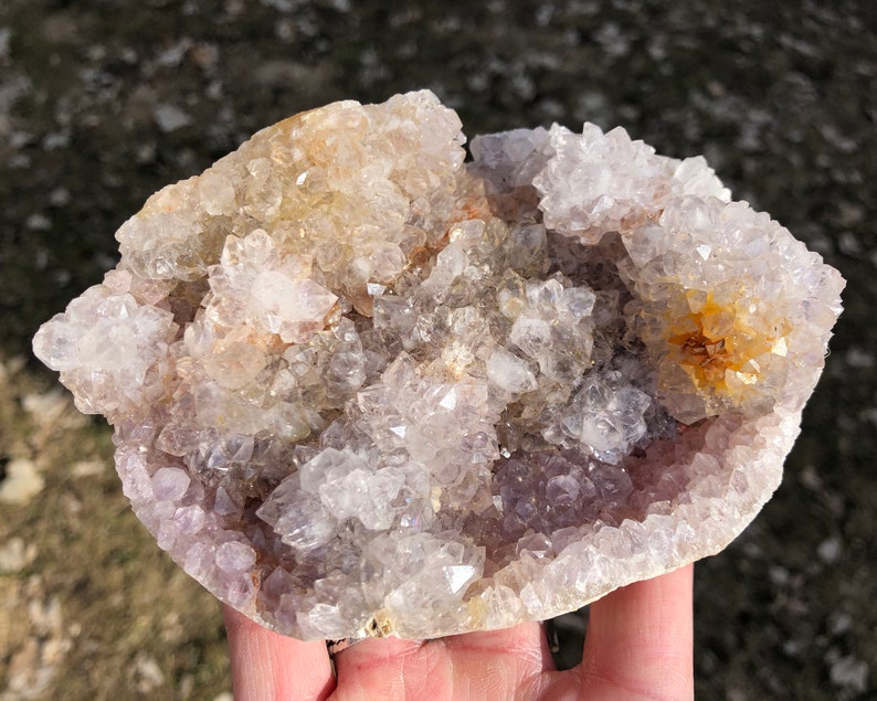 K&ouml;nnte beinhalten: Eine gro&szlig;e Amethyst-Geode mit einem Cluster aus klaren Quarzkristallen oben. Die Geode ist mit kleineren Amethystkristallen gef&uuml;llt und hat ein nat&uuml;rliches, raues &Auml;u&szlig;eres.