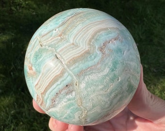 May include: A large, green, white, and brown banded sphere made of polished agate. The sphere has a natural crack running through it.