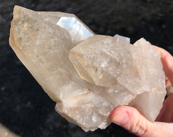 May include: A large cluster of clear quartz crystals with a milky white hue. The crystals are clustered together in a natural formation, with some showing signs of inclusions.
