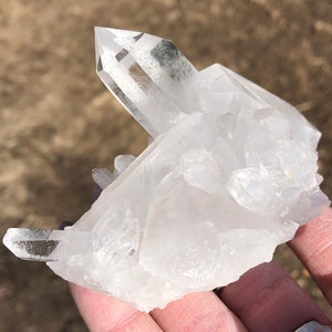 May include: A cluster of clear quartz crystals with a variety of sizes and shapes. The crystals are arranged in a natural formation, with some pointing upwards and others pointing downwards. The crystals are translucent and have a slight sparkle.