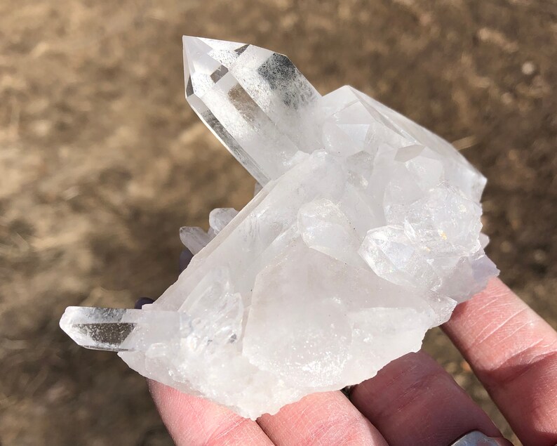 May include: A cluster of clear quartz crystals with a variety of sizes and shapes. The crystals are arranged in a natural formation, with some pointing upwards and others pointing downwards. The crystals are translucent and have a slight sparkle.