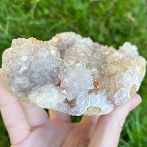 K&ouml;nnte beinhalten: Ein Cluster aus wei&szlig;en und hellvioletten Amethystkristallen mit einer nat&uuml;rlichen, rauen Textur. Die Kristalle sind in einem Cluster angeordnet, wobei einige der Kristalle nach oben und andere nach unten zeigen. Die Kristalle sind durchscheinend und haben einen leichten Schimmer.