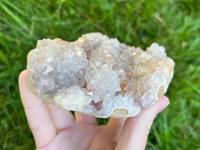 K&ouml;nnte beinhalten: Ein Cluster aus wei&szlig;en und hellvioletten Amethystkristallen mit einer nat&uuml;rlichen, rauen Textur. Die Kristalle sind in einem Cluster angeordnet, wobei einige der Kristalle nach oben und andere nach unten zeigen. Die Kristalle sind durchscheinend und haben einen leichten Schimmer.