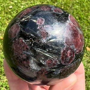 May include: Black sphere with red and gold inclusions. The sphere is polished and smooth.