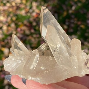 Puede incluir: Un c&uacute;mulo de cristales de cuarzo transparentes de diferentes tama&ntilde;os y formas. Los cristales est&aacute;n dispuestos en un c&uacute;mulo, con algunos apuntando hacia arriba y otros hacia abajo. Los cristales son transl&uacute;cidos y tienen un ligero brillo.