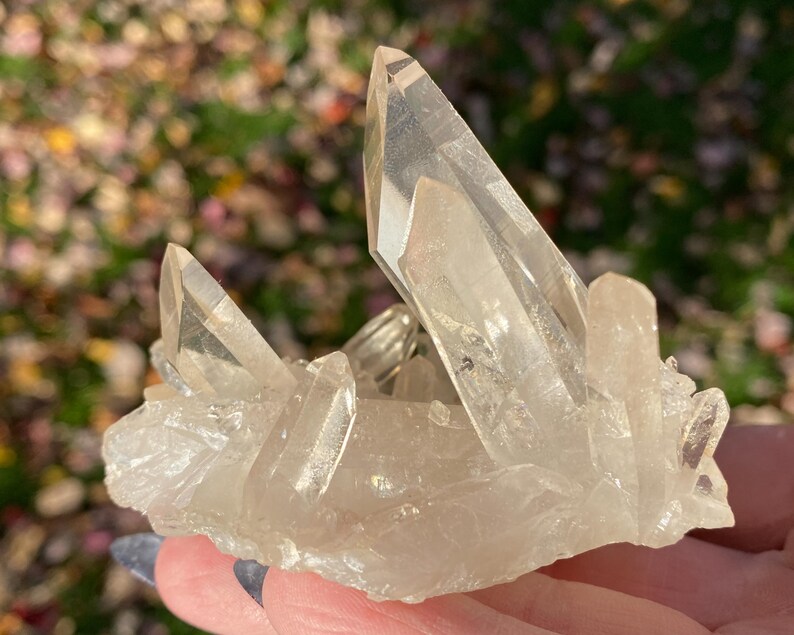 Puede incluir: Un c&uacute;mulo de cristales de cuarzo transparentes de diferentes tama&ntilde;os y formas. Los cristales est&aacute;n dispuestos en un c&uacute;mulo, con algunos apuntando hacia arriba y otros hacia abajo. Los cristales son transl&uacute;cidos y tienen un ligero brillo.