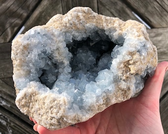 May include: A geode with a large opening revealing a cluster of light blue crystals inside. The geode is surrounded by a rough, tan-coloured exterior.