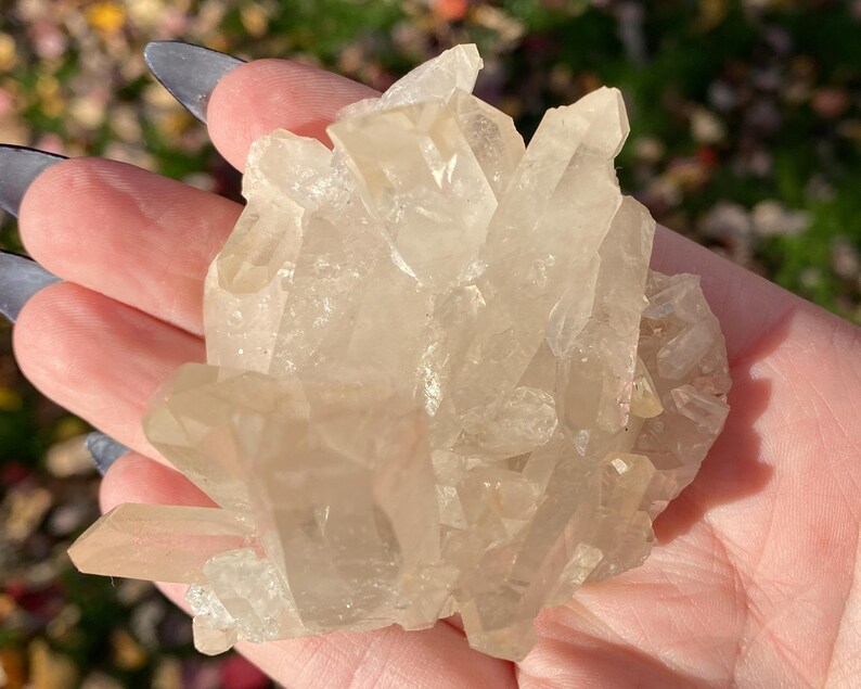 Puede incluir: Un c&uacute;mulo de cristales de cuarzo transparentes con un acabado natural y en bruto. Los cristales est&aacute;n agrupados en una forma tosca y org&aacute;nica, con algunos puntos que se extienden hacia afuera. Los cristales son transl&uacute;cidos y tienen un ligero brillo.