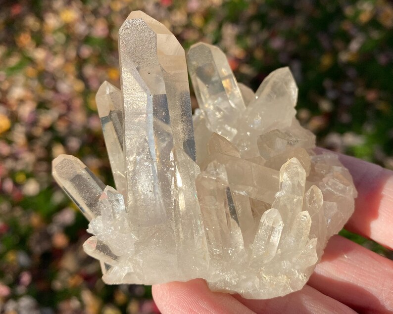 Puede incluir: Un c&uacute;mulo de cristales de cuarzo transparentes de diferentes tama&ntilde;os y formas. Los cristales est&aacute;n dispuestos en una formaci&oacute;n natural, con algunos apuntando hacia arriba y otros hacia abajo. Los cristales son transl&uacute;cidos y tienen un ligero brillo.