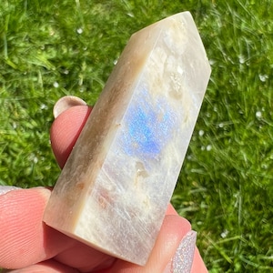 Pode incluir: Uma ponta de pedra da lua branca e iridescente com um brilho azul. A ponta é lisa e polida, e é segurada na mão.