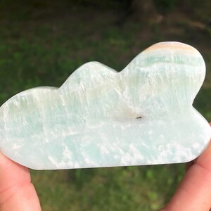 May include: A light blue and white carved celestite crystal shaped like a cloud. The crystal has a smooth, polished surface.