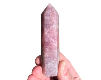 May include: A pale lavender crystal point with a smooth, polished surface. The crystal is shaped like a pyramid with a pointed top and a flat base.