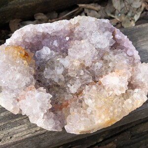 K&ouml;nnte beinhalten: Eine gro&szlig;e Amethyst-Geode mit einem Cluster aus klaren Quarzkristallen. Die Geode ist teilweise ge&ouml;ffnet und zeigt die Amethystkristalle im Inneren. Die Geode liegt auf einem St&uuml;ck verwittertem Holz.