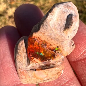 Puede incluir: Una figurita de rana tallada en piedra con una gran pieza de ópalo naranja incrustada en su espalda.