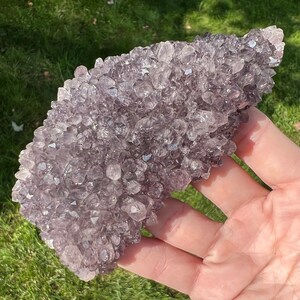 May include: A large amethyst cluster with a purple and white color. The cluster is made up of many small crystals that are tightly packed together. The cluster is about 6 inches long and 4 inches wide.