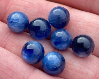 May include: Seven smooth, round, blue gemstone beads. The beads have a light blue color with darker blue streaks throughout.
