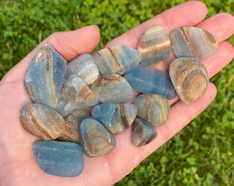 May include: A collection of blue and brown banded agate tumbled stones. The stones are smooth and polished, with a variety of patterns and colors.