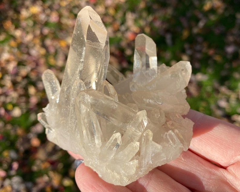 Puede incluir: Un c&uacute;mulo de cristales de cuarzo transparentes de diferentes tama&ntilde;os y formas. Los cristales est&aacute;n dispuestos de forma natural, algunos apuntando hacia arriba y otros hacia abajo. Los cristales son transl&uacute;cidos y tienen un ligero brillo.