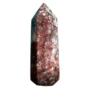 Könnte beinhalten: Eine rote und klare Kristallspitze mit einer rauen, strukturierten Oberfläche. Der Kristall ist pyramidenförmig mit einer spitzen Spitze.