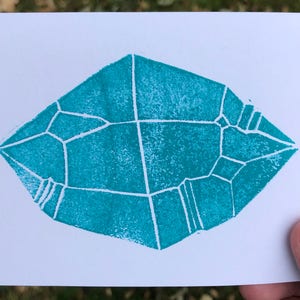 Puede incluir: Una forma geométrica azul turquesa con líneas blancas, que se asemeja a un cristal, impresa sobre un fondo blanco.