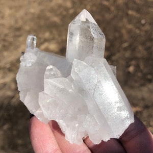 May include: A cluster of clear quartz crystals with a variety of shapes and sizes. The crystals are arranged in a natural formation, with some of the points facing upwards.