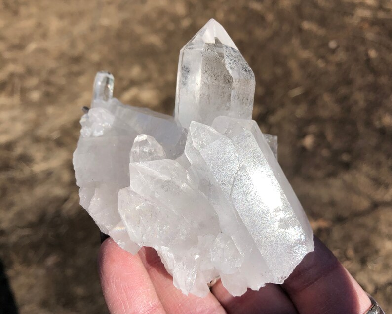May include: A cluster of clear quartz crystals with a variety of shapes and sizes. The crystals are arranged in a natural formation, with some of the points facing upwards.