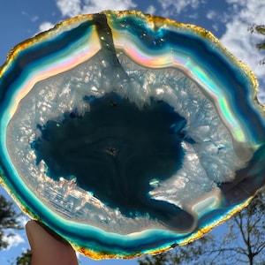 May include: A large, iridescent agate slice with a blue and white centre and a golden rim. The agate is translucent and shows a rainbow of colours in the light.