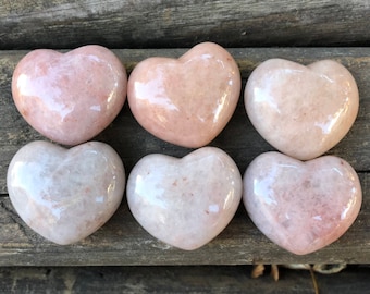 May include: Six polished heart-shaped stones in varying shades of pink and white. The stones have a smooth, glossy finish and are arranged in two rows of three. The hearts are likely made of a natural material.