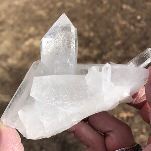 May include: A large, clear quartz crystal cluster with multiple points. The crystal is translucent and has a natural, rough texture.
