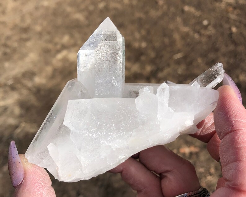 May include: A large, clear quartz crystal cluster with multiple points. The crystal is translucent and has a natural, rough texture.