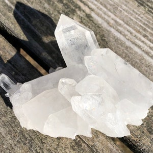 May include: A cluster of clear quartz crystals with a variety of sizes and shapes. The crystals are arranged in a natural formation, with some pointing upwards and others pointing downwards. The crystals are translucent and have a slight sparkle.