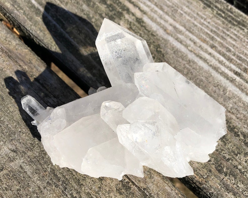 May include: A cluster of clear quartz crystals with a variety of sizes and shapes. The crystals are arranged in a natural formation, with some pointing upwards and others pointing downwards. The crystals are translucent and have a slight sparkle.